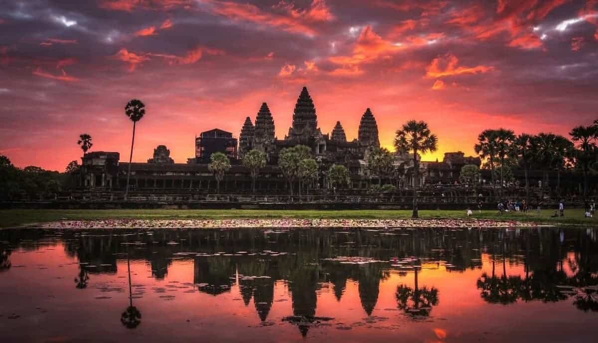 Angkor Wat temple at sunset with vibrant sky and reflection in water.