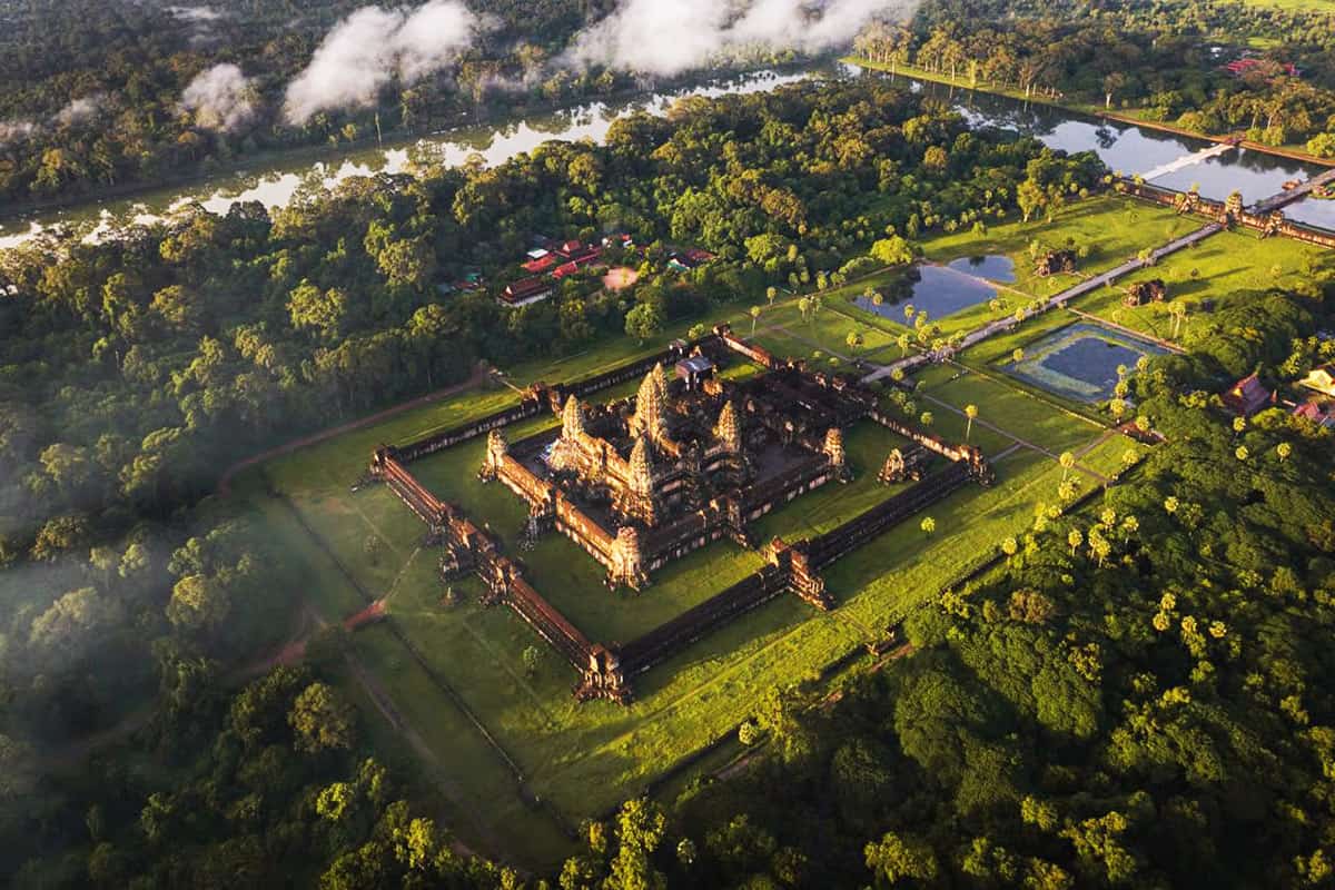 Aerial view of an ancient temple surrounded by lush greenery and water bodies in a tropical jungle s.
