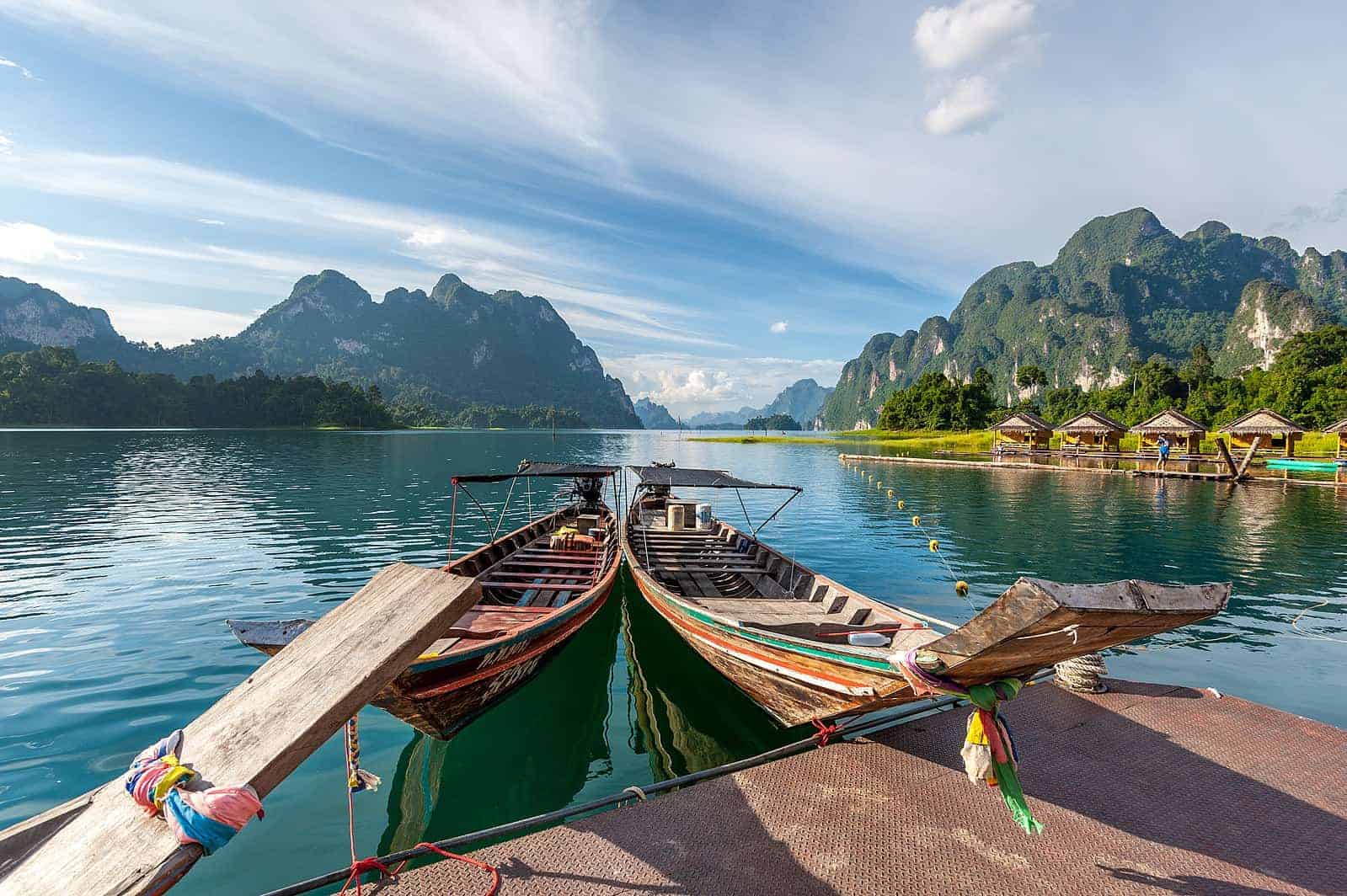 Traditional longtail boats on a serene river surrounded by lush mountains in Thailand.