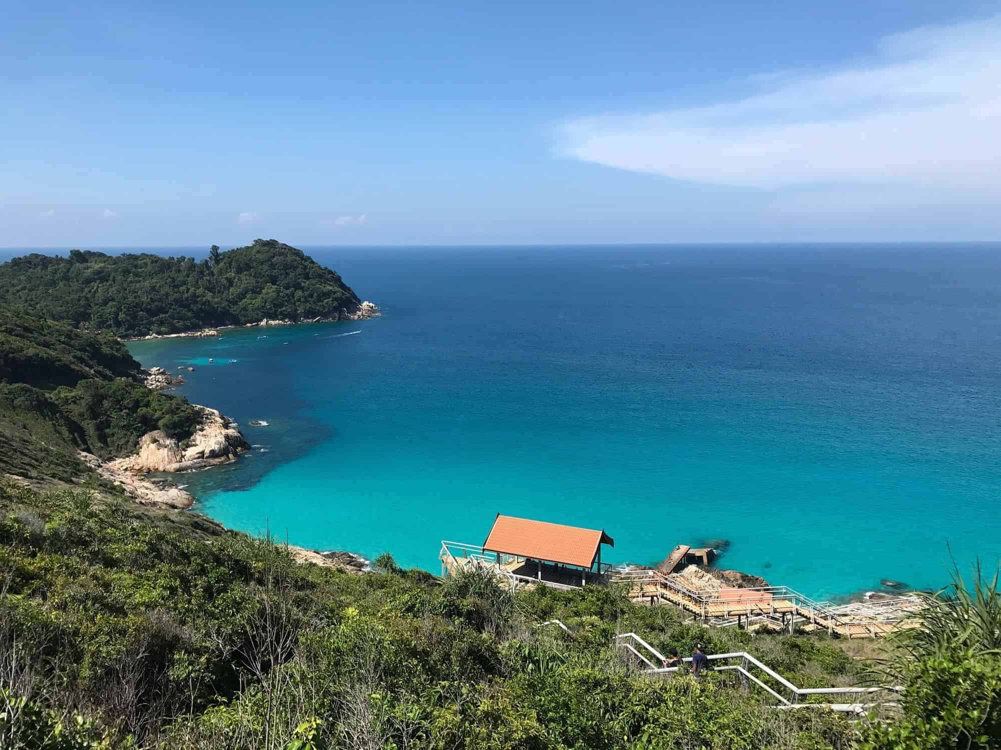 Beachside cottage with turquoise waters and lush green hills, perfect for relaxing vacations.