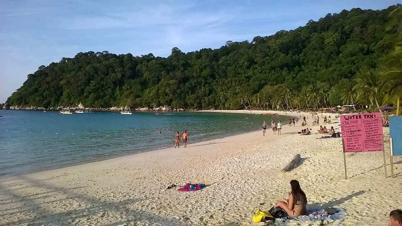 Beach with lush green hills and visitors relaxing by the water.